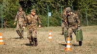 Ein Soldat rennt mit zwei großen Benzinkanistern in den Händen, ein Ausbilder treibt ihn an.