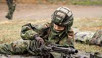Eine Soldatin liegt auf der Wiese und zerlegt abgestützt ein MG3.
