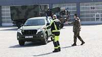 Ein Feuerwehrmann und ein Soldat halten ein militärisches Fahrzeug an, um es einweisen zu können.