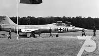 Ein Kampfjet steht auf dem Flugfeld. Mehrere Soldaten stehen davor.