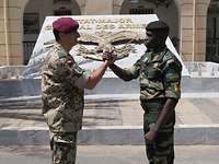 Zwei Soldaten reichen sich draußen vor einem Gebäude mit Skulptur symbolisch die Hand.