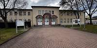 Zweigeschossiges, beigefarbenes Gebäude mit je einem halbrunden Vordach über drei Eingängen 