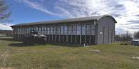Längliche, anthrazitfarbene Halle mit großem Fenstern und Halbtonnendach