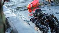 Ein Marinetaucher steigt aus dem Wasser in ein Schlauchboot.