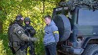 Ein Soldat und eine Soldatin stehen mit einem jungen Mann an einem militärischen Fahrzeug