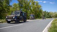 Militärische Fahrzeuge – ein Pkw, ein Lkw und ein Motorrad – stehen auf einer Landstraße