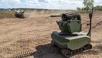 Unbemanntes Kettenfahrzeug der Bundeswehr mit Waffensystem rollt über Sand.