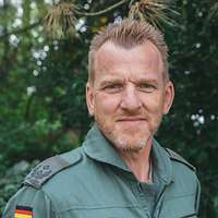 Ein Soldat lächelt vor einem Busch
