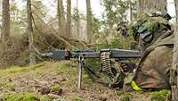 Ein Soldat liegt im Wald am Boden mit der Waffe im Anschlag.
