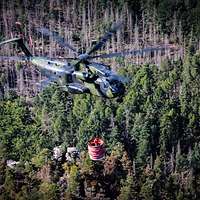 Ein Bundeswehr-Hubschrauber der einen großen Wassertank transportiert und damit Waldbrände löscht