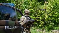 Ein Soldat steht vor einem militärischen Fahrzeug, vor ihm fliegt eine Drohne