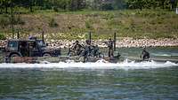Militärfahrzeuge und Soldaten überqueren auf einer militärischen Fähre einen Fluss