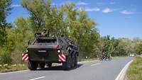 Ein Panzer fährt auf einer Landstraße. Aus der Luke schaut ein bewaffneter Soldat