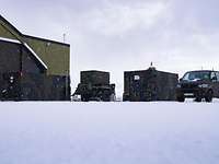 Ein Containerkomplex auf einem mit Schneebedeckten Gelände mit einem Militär-Transporter.