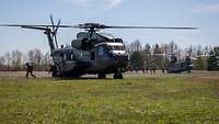 Soldaten verlassen eine CH-53 und eine CH-47, die mit laufenden Rotoren auf einer Grasfläche stehen.