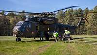 Zwei Soldaten tragen einen Tankschlauch zu einer CH-53, die auf einer Lichtung steht.