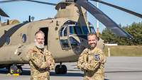 Zwei Soldaten, ein Deutscher und ein Niederländer, stehen gemeinsam vor einem Hubschrauber.