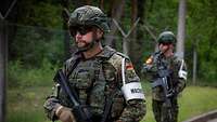 Zwei bewaffnete Soldaten mit weißen Armbinden, darauf das Wort Wache, laufen Streife.