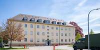 Länglicher, hellgelber, dreigeschossiger Block mit Walmdach, darin Fenster
