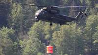 Ein Militärhubschrauber schwebt über einem See und nimmt mit einem Behälter Wasser auf