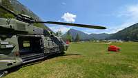 Ein Militärhubschrauber steht am Boden, neben ihm liegt ein orangener Behälter für Löschwasser