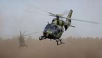 Zwei Hubschrauber im Flug. Staub liegt in der Luft.