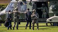 Ein militärischer Hubschrauber steht auf einer Wiese. 5 Personen stehen darin bzw davor.