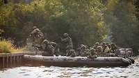 Soldatinnen und Soldaten verlassen am befestigten Ufer eines Flusses ein Schlauchboot.
