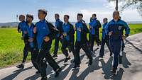 Etwa ein Dutzend Soldatinnen und Soldaten in blauen Sportanzügen joggen über Asphalt.