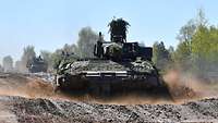 Im Vordergrund fährt ein Schützenpanzer durch den Schlamm, der überall hin spritzt.