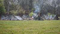 Mehrere Zelte im Flecktarnmuster um ein Feuer aufgestellt.