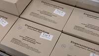 Mehrere graue Kartons mit der Aufschrift „Einpersonenpackung Typ 9“ liegen nebeneinander.