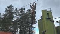 Ein Soldat steht hangelt sich am Höhenhindernis über einen Seilsteg.