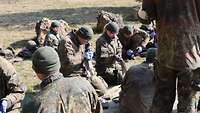 Mehrere Soldaten hocken auf einer Wiese und reinigen nach der Ausbildung ihre Gewehre.