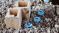 Holzklötzer mit Nummern und blaue taktische Zeichen aus Plastik liegen auf Kiessteinen.