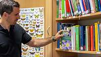 Ein Mann steht im Seitenprofil vor einem Bücherregal mit Fachliteratur zu Pflanzen und Tieren.