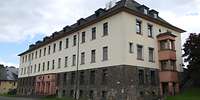 Viergeschossiges Gebäude mit Feldsteinsockel, hellem Anstrich, Walmdach und Balkonanbau