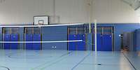 Blick in die Sporthalle mit einem Volleyballnetz mit hellblauem Boden und blauer Wand