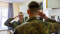 Zwei Soldaten grüßen sich mit flacher Hand an der Stirn vor einem Spind in einem Raum.