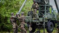 Soldaten eines IT-Bataillons bauen eine große, auf einem Anhänger befindliche Antenne auf.