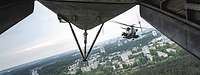 Hinter der geöffneten Heckklappe eines Hubschraubers fliegt ein zweiter Helikopter über einer Stadt.