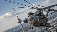 Ein Militärhubschraubers des Typ CH-53 fliegt an einem Funkturm vorbei über eine Stadt in Litauen.