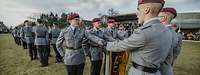 Soldaten stehen in Gruppen auf einer Wiese und sprechen mit der linken Hand an der Truppenfahne.