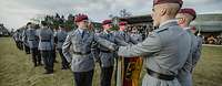 Soldaten stehen in Gruppen auf einer Wiese und sprechen mit der linken Hand an der Truppenfahne.