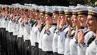 Mehrere Soldaten stehen in Reihen mit erhobener Hand und sprechen.