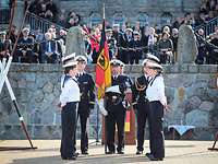 Sechs Soldaten stehen an der Truppenfahne vor einer Feldsteinmauer und Publikum.
