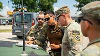 Geparktes Fahrzeug, wo drei Soldaten mit einer Karte davor stehen und sich unterhalten
