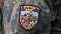 Ein Patch auf Flecktarn mit der Aufschrift Bollwerk Bärlin 2026 zeigt einen brüllenden Bären vor dem Brandenburger Tor