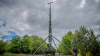 Soldaten stehen vor einem aufgebauten Antennenmast.