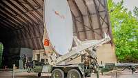 Die große weiße SATCOM-Schüssel ist im alten Flugzeughangar aufgebaut.